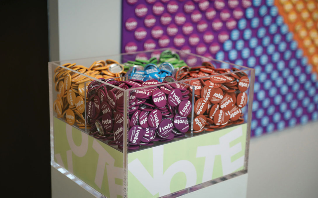 Purple, yellow, orange, blue, and green round voting pins rest in an acrylic box.