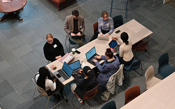 Above shot of seven students sitting around a rectangle in the Great Hall. They have laptops open and are engaged in discussion.