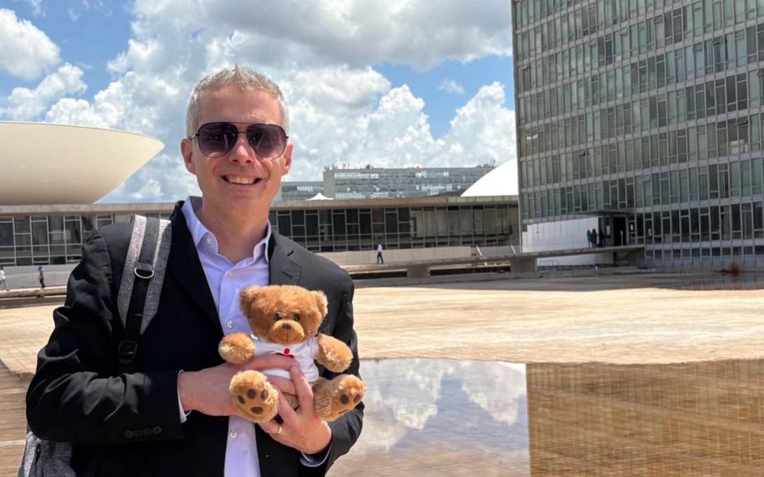 An individual holding a teddy bear in front of the National Congress of Brazil in Brasília.