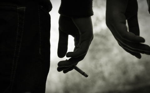 Close-up black and white photo of two people, their hands near each other and one holding a smoldering cigarette