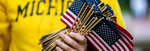 Photo of a person in a Michigan sweatshirt holding a bundle of small handheld American flags (credit: Michigan Photography)