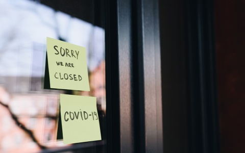Two post-it notes on a business' front door, reading "Sorry we're closed" and "COVID-19"