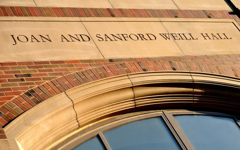 A close-up photo of the entrance to Weill Hall, with "Joan and Sanford Weill Hall" etched into the stone and light reflecting off the large glass windows