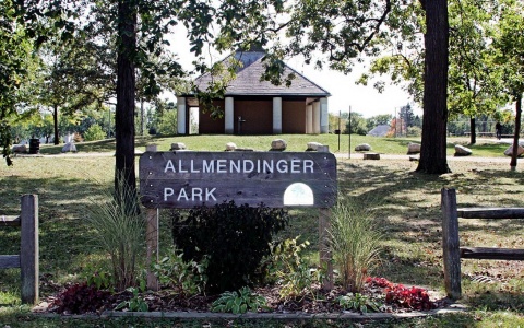 Photo of an entrance sign for Allmendinger Park with a public building and the park in the background