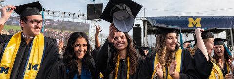 Photo of new BA graduates tossing their mortar boards into the air in celebration (Photo by Michigan Photography)