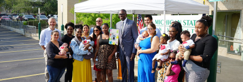 Group of adults and babies posing with an award certificate in front of a Michigan State University extension sign.