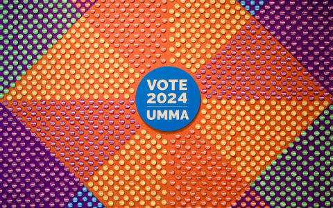 A geometric wall of multi-colored buttons. The blue circle in the middle says "Vote 2024 UMMA."