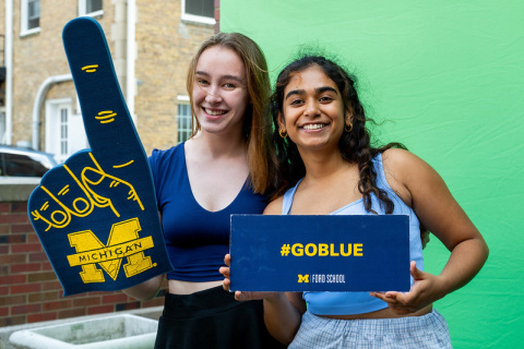 Two students smile and hold up University of Michigan signage 