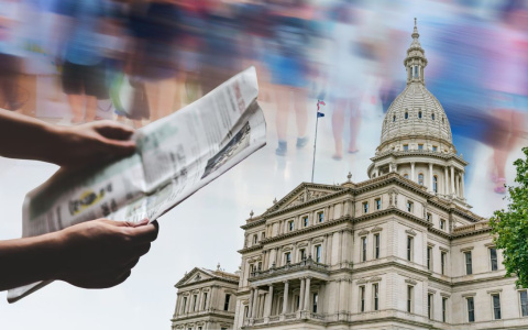 hands holding a newspaper in front of the michigan capitol building