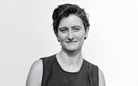 Black and white portrait of a smiling person with short hair, wearing a sleeveless top, against a plain background.